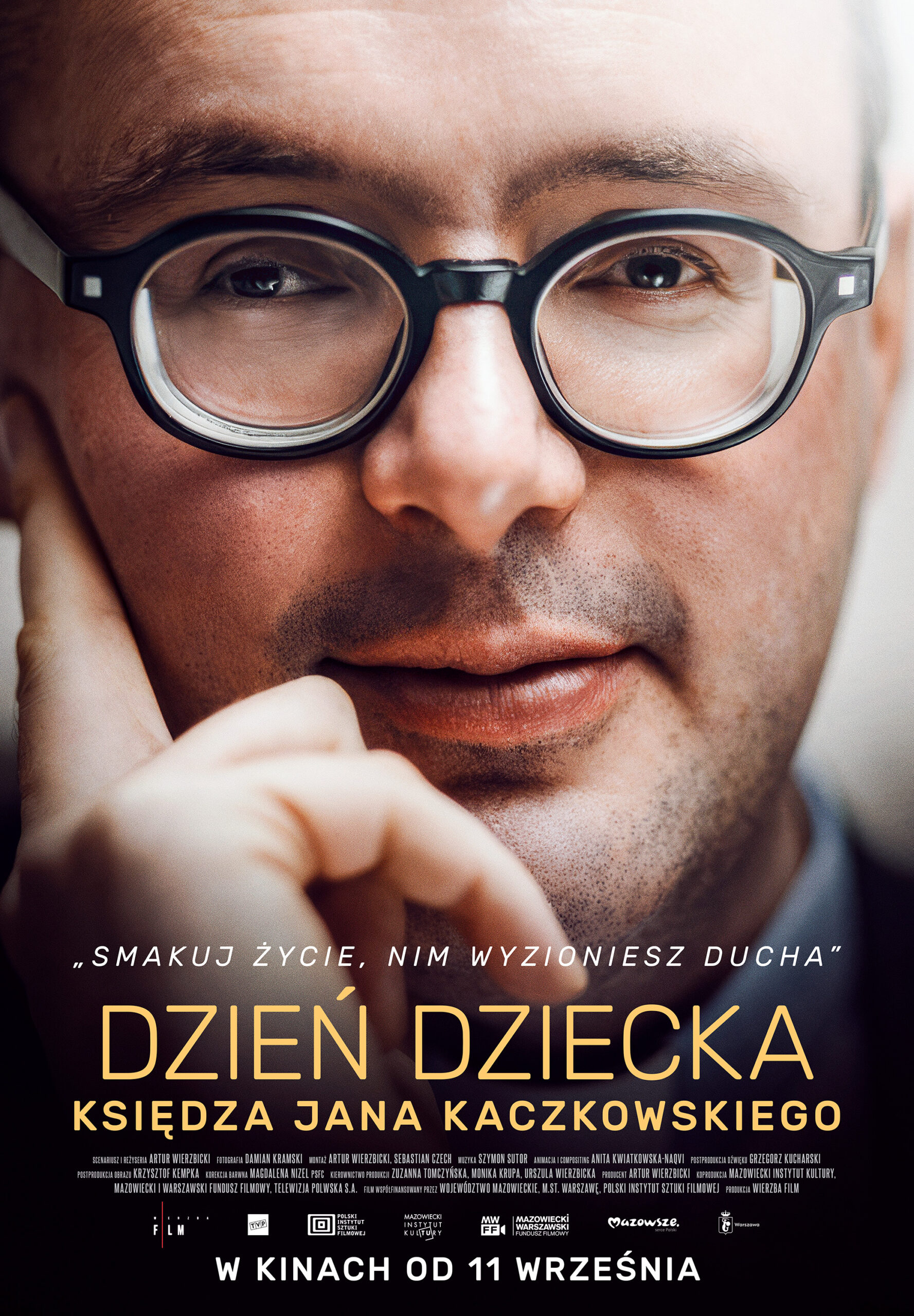 Zbliżenie na uśmiechniętego mężczyznę w okrągłych okularach, plakat filmu Dzień Dziecka Księdza Jana Kaczkowskiego, GO KINO Oława